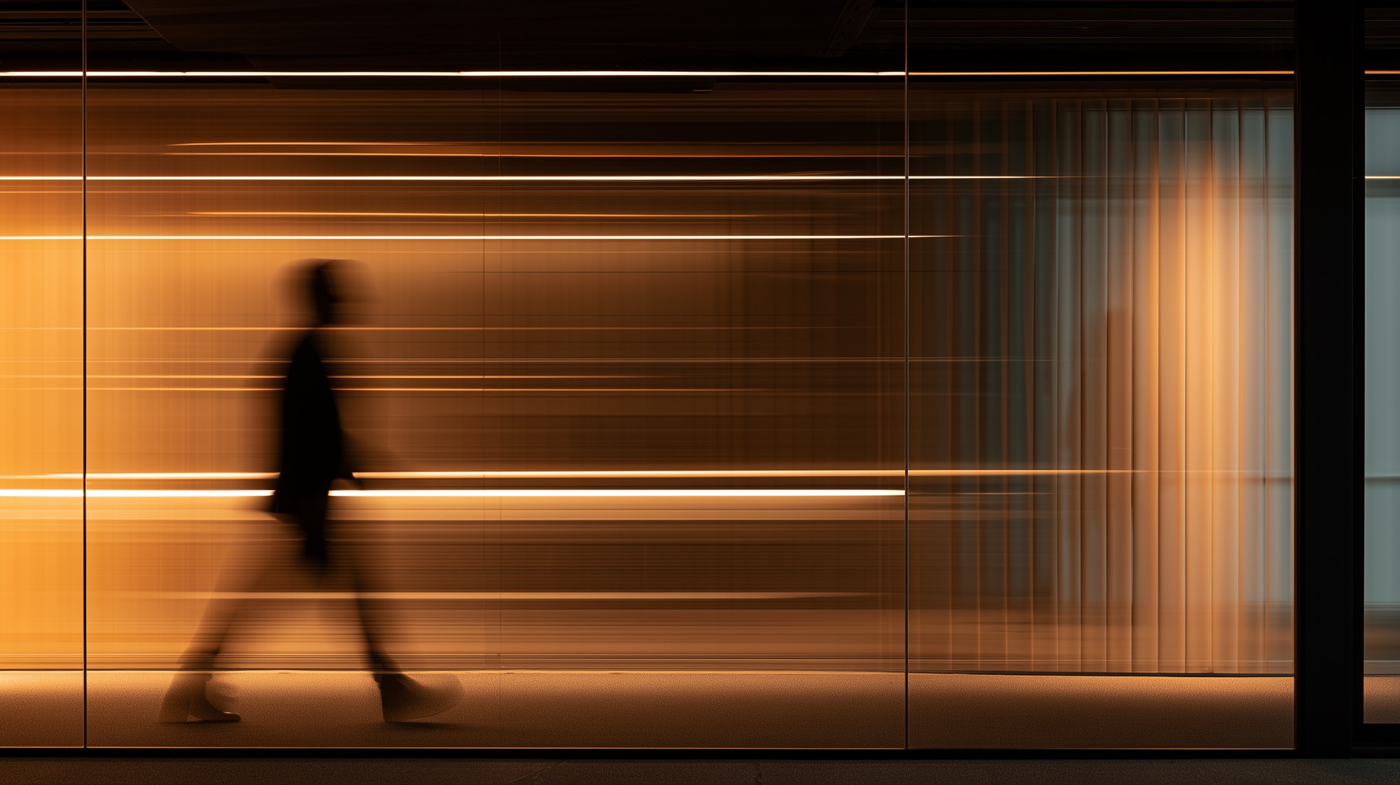 A figure passing a lit glass façade